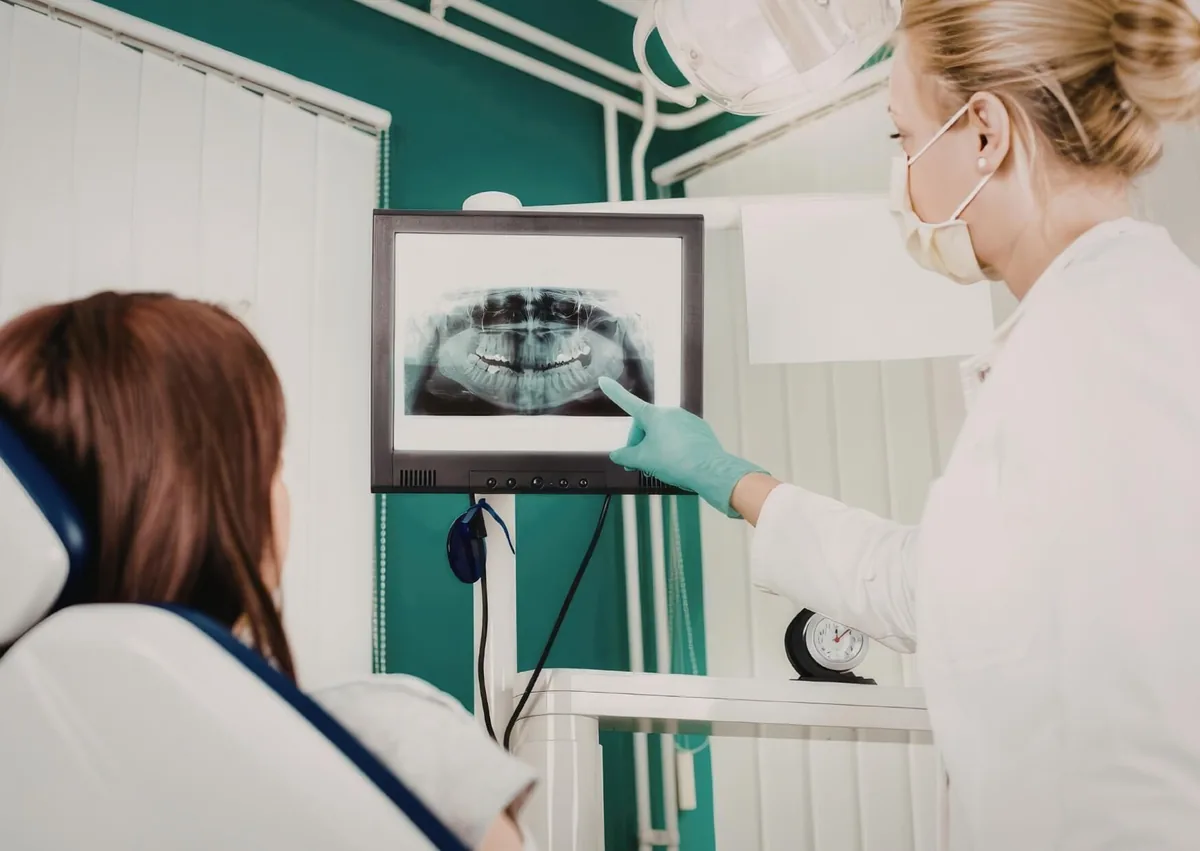 Dentist reviewing a panoramic dental X-ray with a patient to evaluate bone structure and plan implant restorations.
