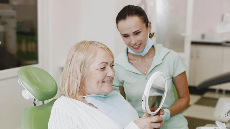a elder woman looking at her new smile using a handheld mirror