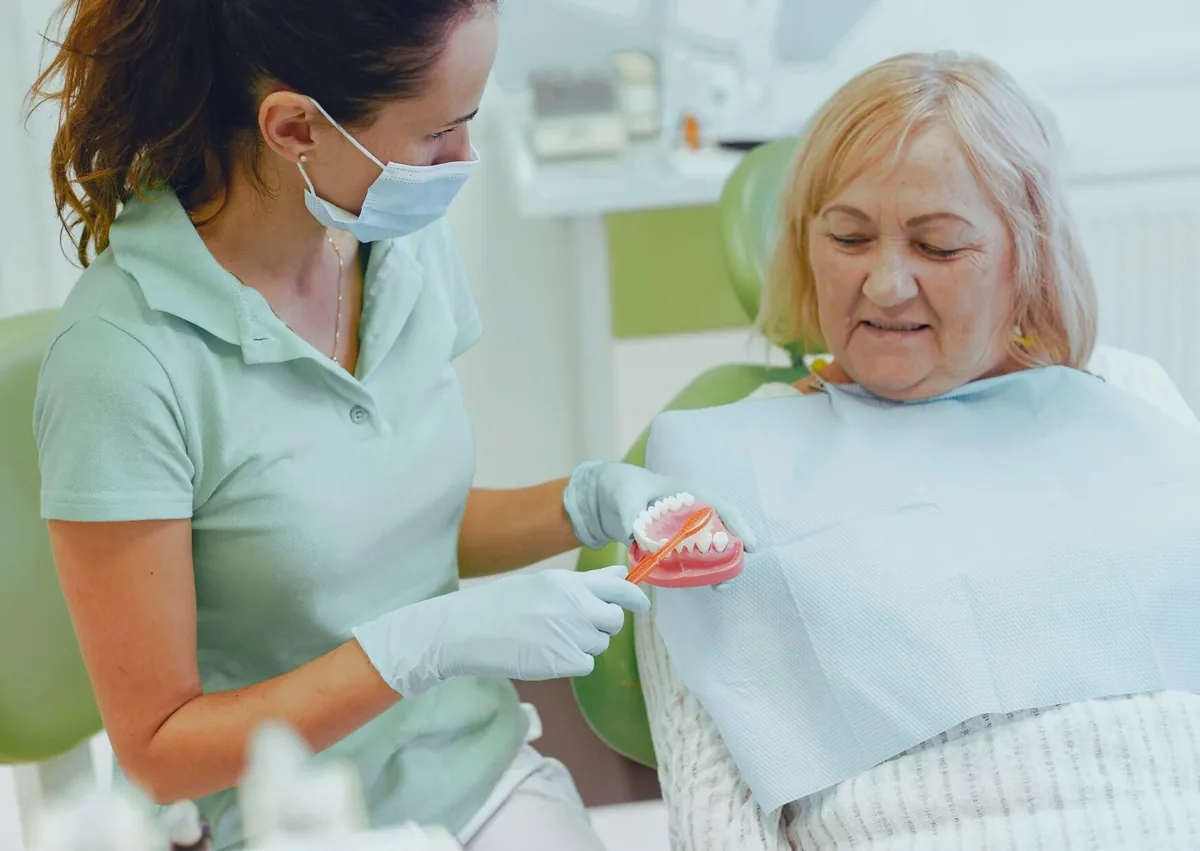 Dental professional explaining denture options and costs to a senior patient using a model of removable dentures.